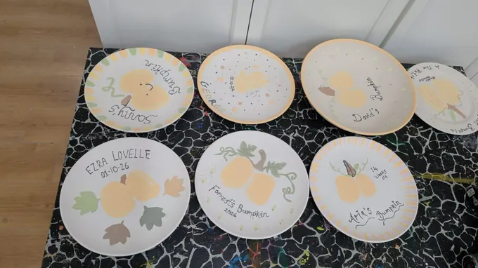 Eight Baby Bumpkin plates, each with a baby’s pumpkin-shaped bottom print and a name