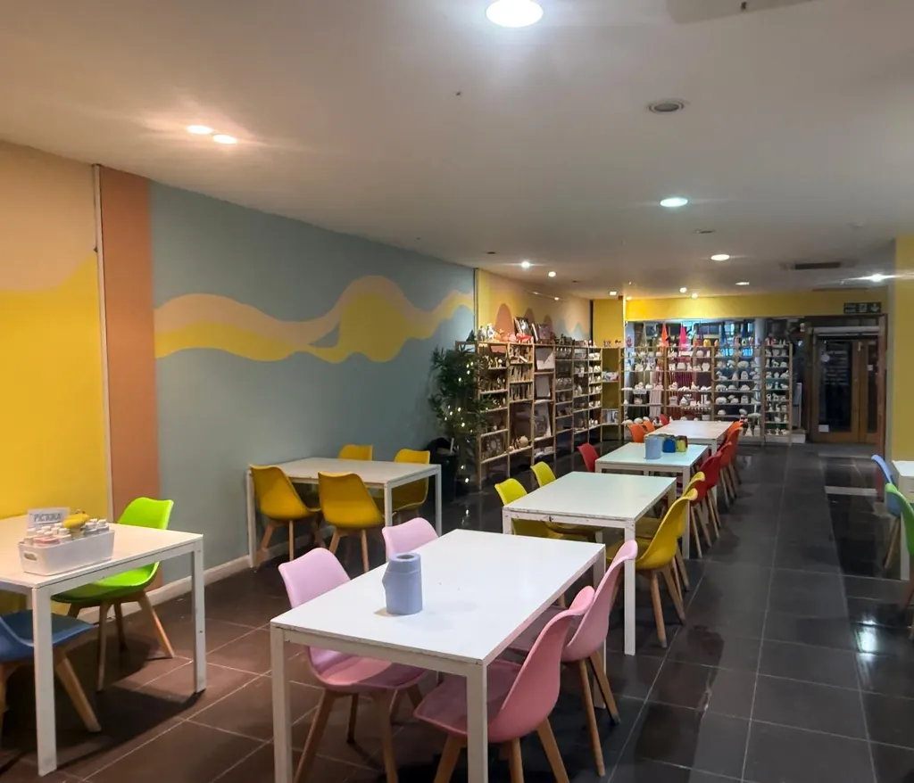 The Pictura creative café: white tables with pink and yellow chairs, colourful painted walls and shelves of pottery to paint