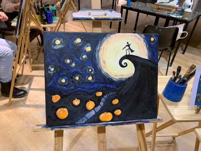 A finished canvas of a starry night with a crescent moon on an easel in the studio