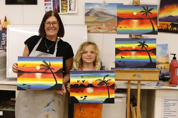 A mum and daughter holding up their sunset canvas paintings in the studio
