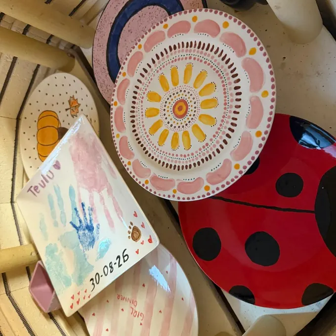 A keepsake tile with a baby’s blue and pink handprints, dated 30-03-26, among freshly fired pottery