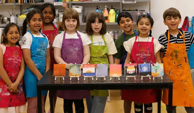 Children in aprons holding up their mini canvas paintings at a Pictura children’s party