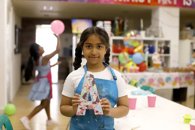 A girl holding up her decoupaged letter at a Pictura party