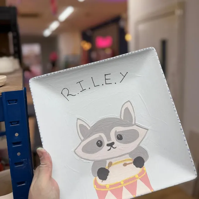 A square plate painted with a raccoon and the name RILEY