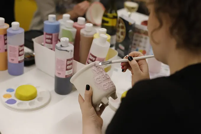A guest painting a pottery piece, with glaze bottles on the table