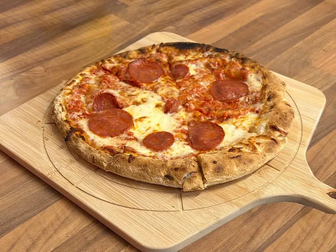 A freshly baked pepperoni pizza on a wooden peel in the Pictura café kitchen